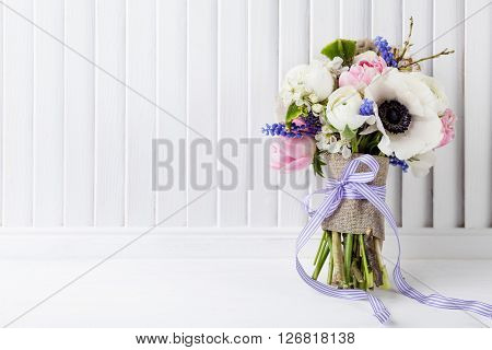 Bouquet from pink tulips violet grape hyacinths white anemones violet veronica and white buttercup with violet ribbon on white wooden shutter background