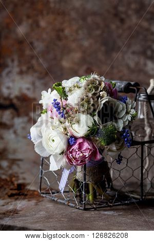 Bouquet from pink tulips violet grape hyacinths white anemones violet veronica and white buttercup with violet ribbon lying in the metal basket with glass bottle in rought rusty metal environment