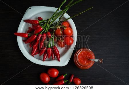 Tomato ketchup hot sauce with chili pepper and cherry tomatoes in a small glass jar. Appetizer of red pepper and tomato sauce - lecho on wooden background. Top view. Copy space.