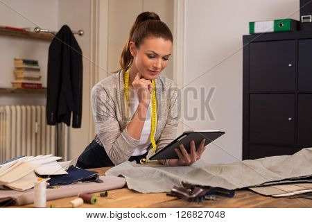 Fashion designer using digital tablet computer in the studio. Young seamstress working on digital tablet for dress designs. Tailor thinking about a design with the help of tablet computer. 