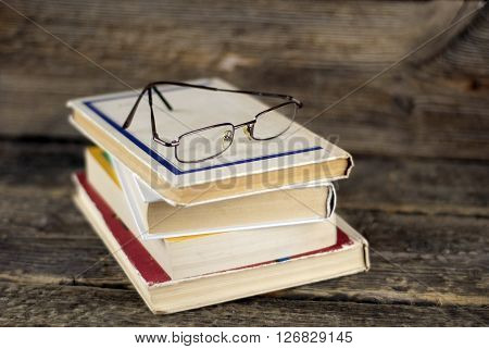 Stack of old book and glasses on a wooden background shallow dof