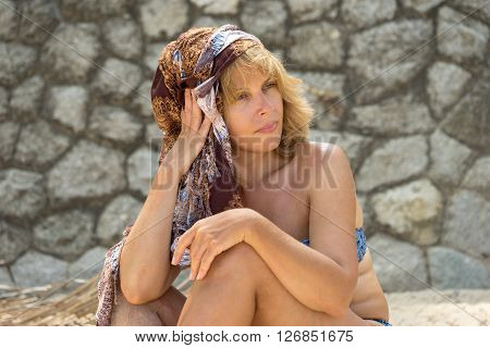 Portrait Of Beautiful Sunburnt Adult Caucasian Woman In Swimsuit And Turban Sitting On The Beach Aga