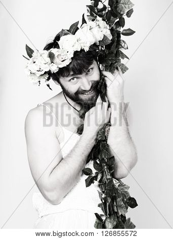 bearded man in a woman's wedding dress on her naked body, clinging to the vine. on his head a wreath of flowers. funny bearded bride, black and white.