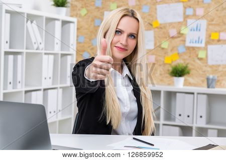 Pretty businesswoman smiling and showing thumbs up in office