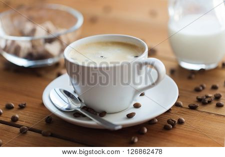 caffeine, objects and drinks concept - close up coffee cup and grains on wooden table