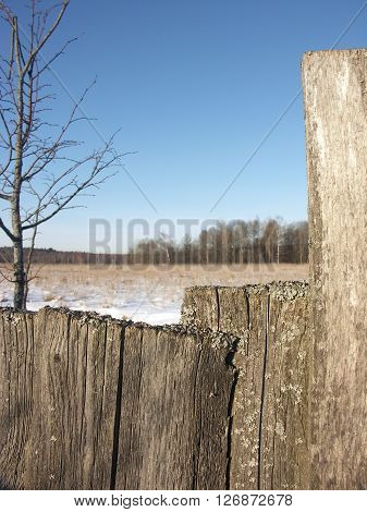 Old wooden fence from boards closeup with snow on top and winter field in the background