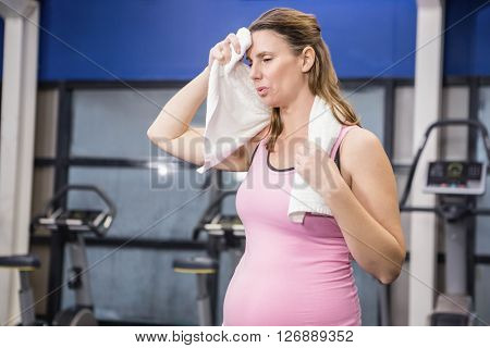 Tired pregnant woman wiping sweat with towel at the gym