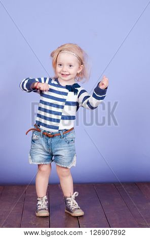 Funny little kids girl 2-3 year old dancing in room over purple. wearing stylish striped shirt and denim shorts. Childhood.