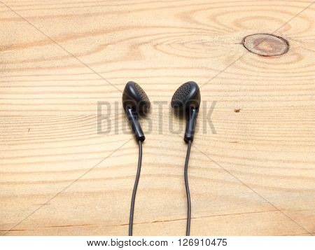 Small black wired earphones lying on a wooden board