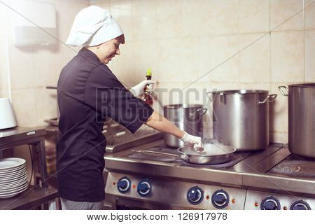 Chef Cooking With Fire In Frying Pan. Professional chef in a commercial kitchen cooking flambe style. Chef frying food in flaming pan on gas hob in commercial kitchen.