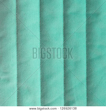 Pastel turquoise quilted textiles with insulation. Vertical stripes. Close up fragment of the top view.