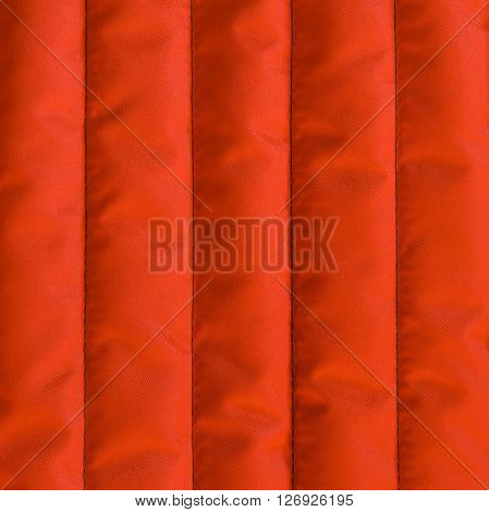 Red orange quilted textiles with insulation. Vertical stripes. Close up fragment of the top view.