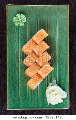 Sushi rolls on a plate with salmon on dark brown wooden table. Side view.
