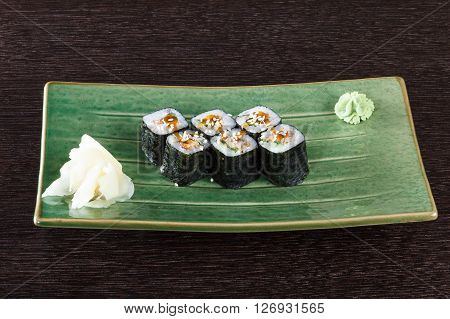 Sushi rolls on a plate with flying fish roe on dark brown wooden table. Side view.