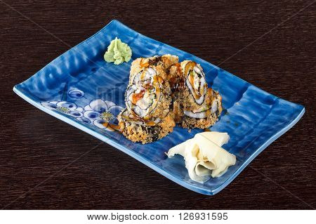 Sushi rolls on a plate with flying fish roe on dark brown wooden table. Side view.
