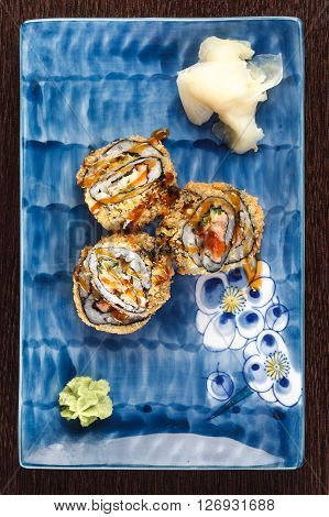 Sushi rolls on a plate with flying fish roe on dark brown wooden table. Side view.