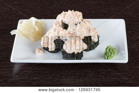 Sushi rolls on a plate with flying fish roe on dark brown wooden table. Side view.