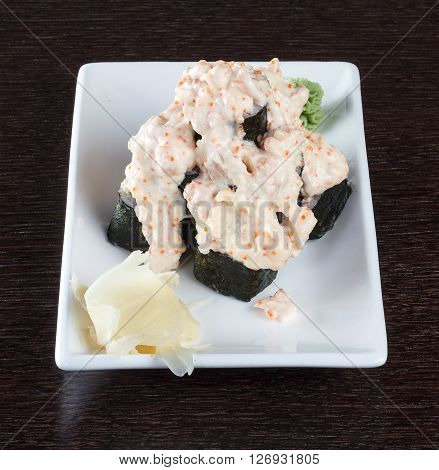 Sushi rolls on a plate with flying fish roe on dark brown wooden table. Side view.