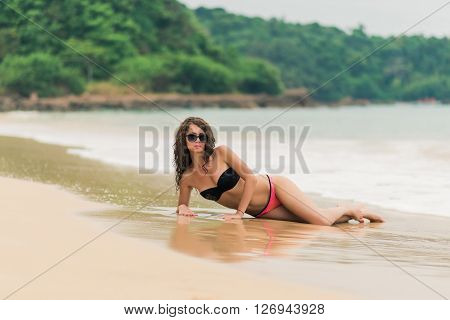 Sexy tanned fit girl in black bikinii on blue ocean background. Young curly hair woman on the tropical beach. Woman in bikini at tropical beach.