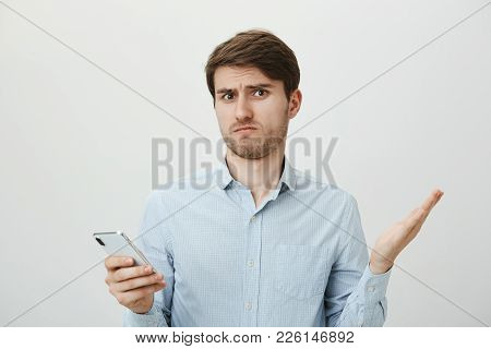Handsome Brunette Guy With Bristle Shrugging And Spreading Hands With Lifted Eyebrows, Expressing Th