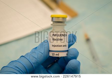 Doctor Holding Influenza Vaccine Vial In Hand With A Syringe At The Background