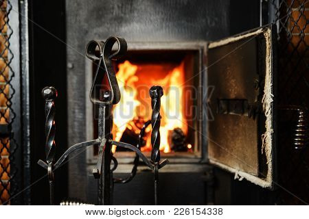 Accessories For Care Of The Stove In Front Of An Open Firebox With A Red Yellow Flame