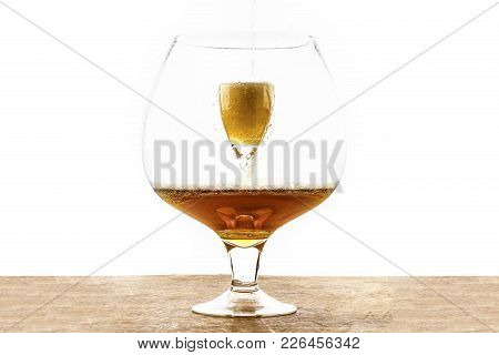 Beer Is Pouring Into A Glass Which Is Into Another Huge Glass, Creating Foam And Bubbles On The Wood