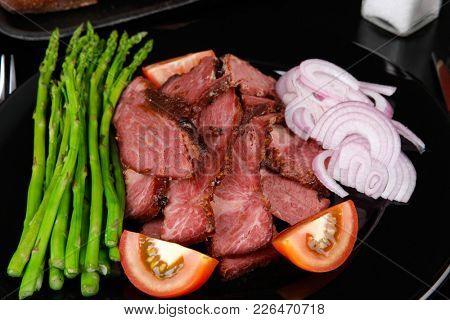 business lunch fresh roast beef meat slices on black plate wotj cutlery asparagus boiled broccoli rye bun on wooden table