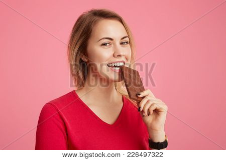 Cheerful Young Beautiful Young Woman Enjoys Sweet Chocolate, Doesn`t Think About Figure, Being In Go