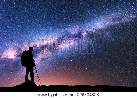 Silhouette Of Man With Backpack And Trekking Poles Against Amazing Purple Milky Way At Night. Space.