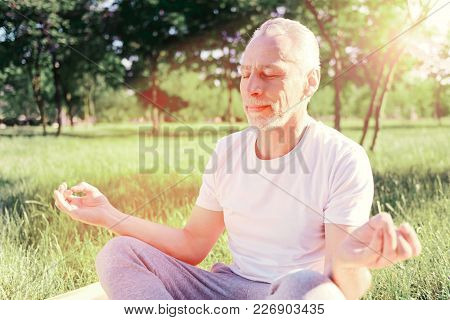 Calmness. Close Up Of Peaceful Man Keeping Fingers Together While Sitting On The Ground Pad And Doin