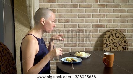 Proper Nutrition After Chemotherapy. A Bald Woman At The Table Drinks Pills While Eating.