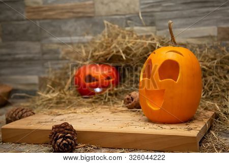 Red And Yellow Halloween Pumpkins Lie On The Hay Against The Background Of A Gray Stone Wall. Cones 