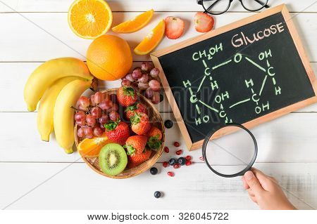 Glucose Molecule On Blackboard With Mixed Fresh Fruits Salad And Little Hand Holding Magnifying Glas