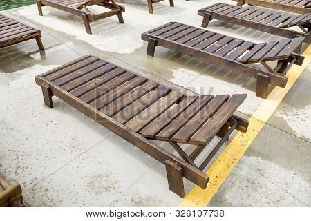 Row Of Empty Wooden Beach Chairs Near Water Outdoors.