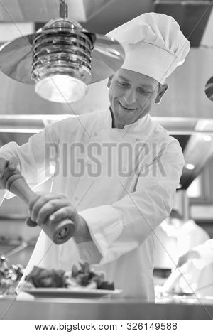 a black and white photograph of a Mature chef using peppermill on salad in plate at restaurant