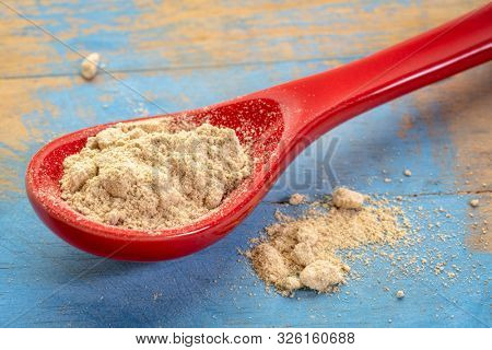 maca root powder on on a red stoneware teaspoon against grunge wood, healthy superfood concept