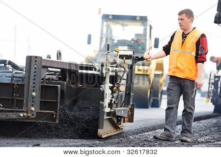 Trabajador operando la máquina pavimentadora de asfalto durante la construcción de carreteras y obras de reparación