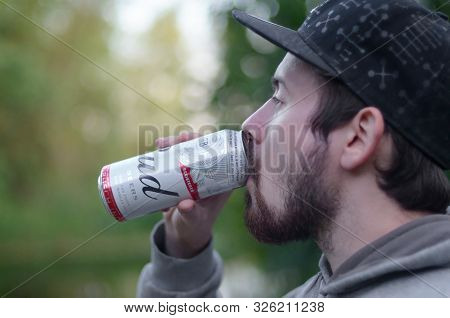 Sumy, Ukraine - August 10, 2019: Young Bearded Man Drinks Budweiser Bud Beer In Aluminium Can On Gre