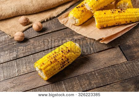 Heap Of Fried Corn Cobs Near Whole Greek Nuts Lies On Crumpled Paper And Old Brown Rustic Wooden Tab