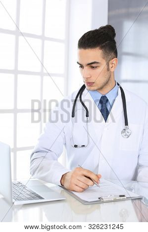 Arab Doctor Man Using Laptop Computer While Filling Up Medication History Records Form At The Glass 