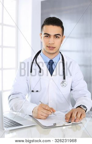 Arab Doctor Man Using Laptop Computer While Filling Up Medication History Records Form At The Glass 