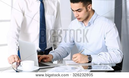 Businessman Working With Computer In Modern Office, Male Colleague At Background . Headshot Of Arab 