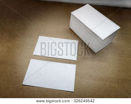 Two Business Cards Lie On A Brown Vintage Surface Near A Pile Of White Blank Visiting Cards. Beautif