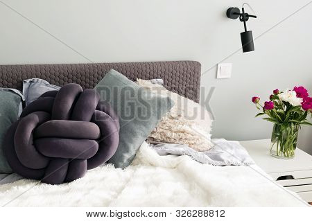 Bed With A Lot Of Decorative Pillows And Peonies On The Night Stand.
