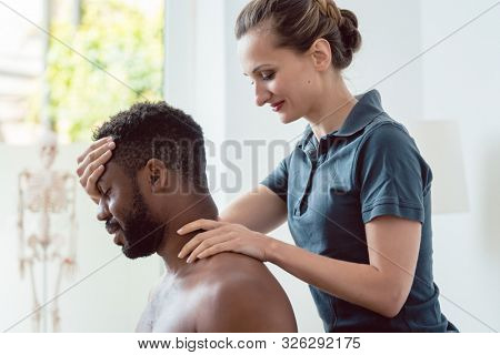 Woman physical therapist massaging young black man holding his head