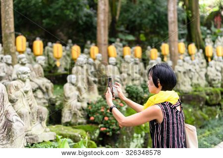 mature Asian woman take a picture at a garden with arhat stone statues