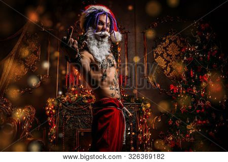Bad Santa concept. Portrait of a nude tattooed Santa with purple dreads demonstrating antisocial behavior, rudeness and aggression. 