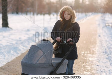 Mom Walk With Baby In Pram. Winter Park. Happy Woman With Her Baby. Mom Using Phone In Winter