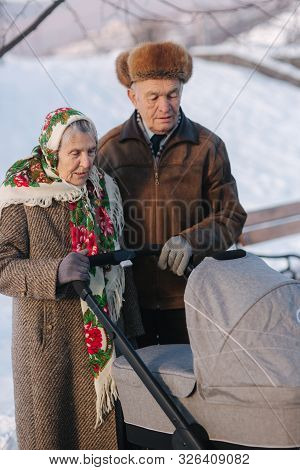 Grand Grandparents Walking With A Baby In Beautiful Pram. Winter Time